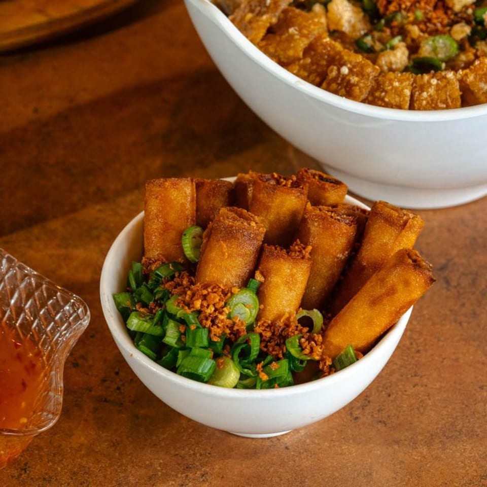 Crispy Filipino lumpia rolls in a white bowl, garnished with green onions and fried garlic.