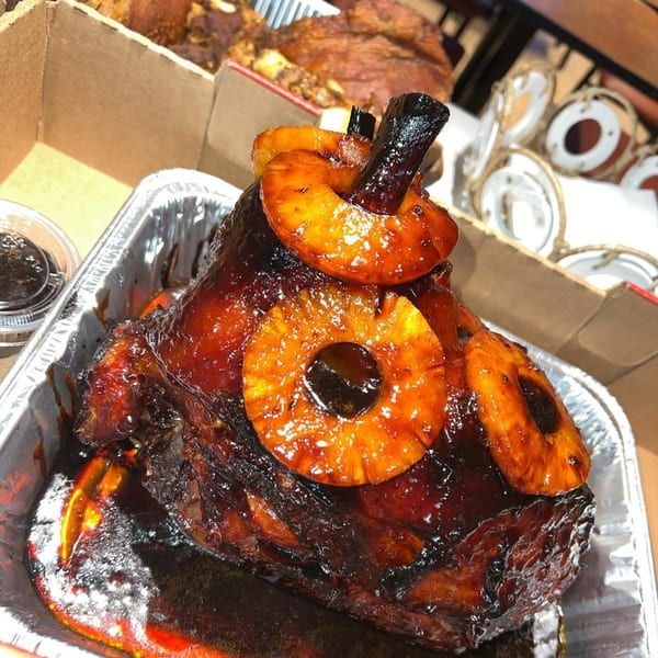 A glazed Filipino ham with pineapple slices and a dark, rich sauce in a foil pan.