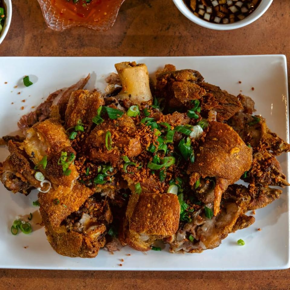 Crispy pata, a Filipino deep-fried pork hock dish, garnished with green onions and garlic on a white plate.