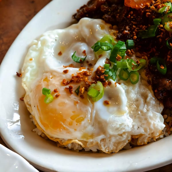 Filipino silog dish with a sunny-side-up egg, garlic rice, and green onions on a white plate.