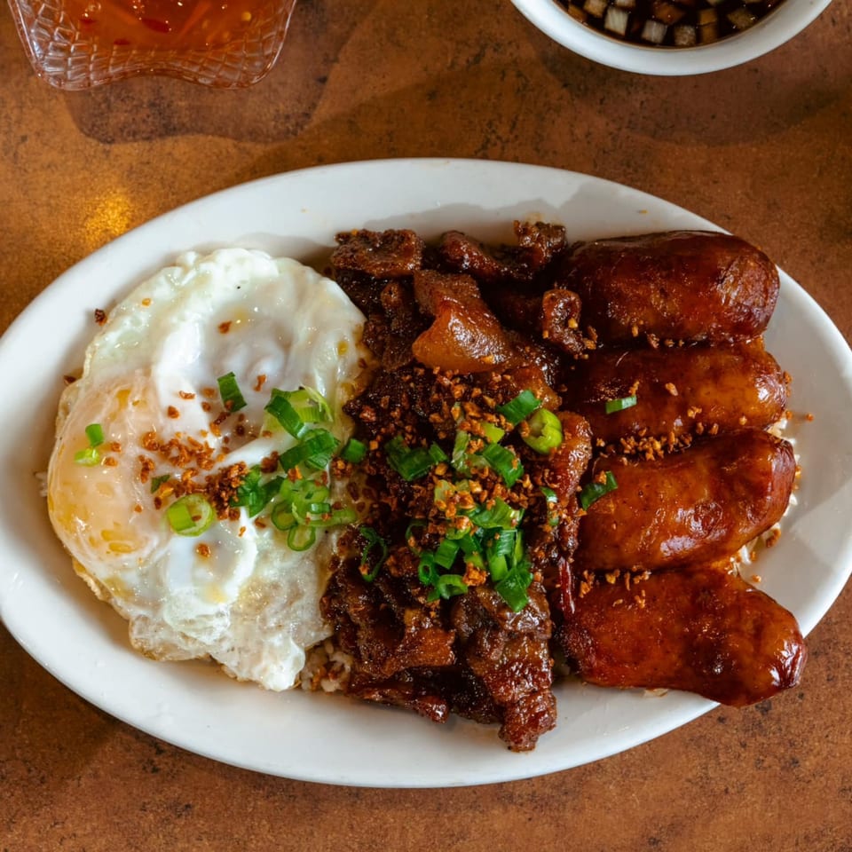 Filipino breakfast plate with fried eggs, longganisa sausages, and beef tapa, garnished with green onions.